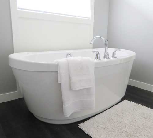 A modern white bathtub with towel over the side